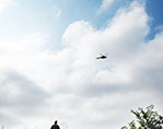 A Performer is flying in a Helicopter Bell 407 and looking at the exhibition from above for 2-3 minutes and then flying away.