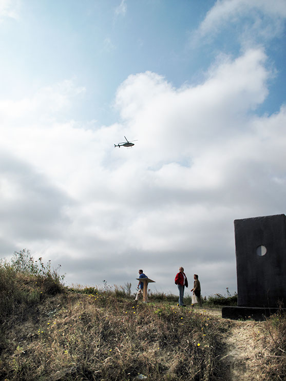 A Performer is flying in a Helicopter Bell 407 and looking at the exhibition from above for 2-3 minutes and then flying away.