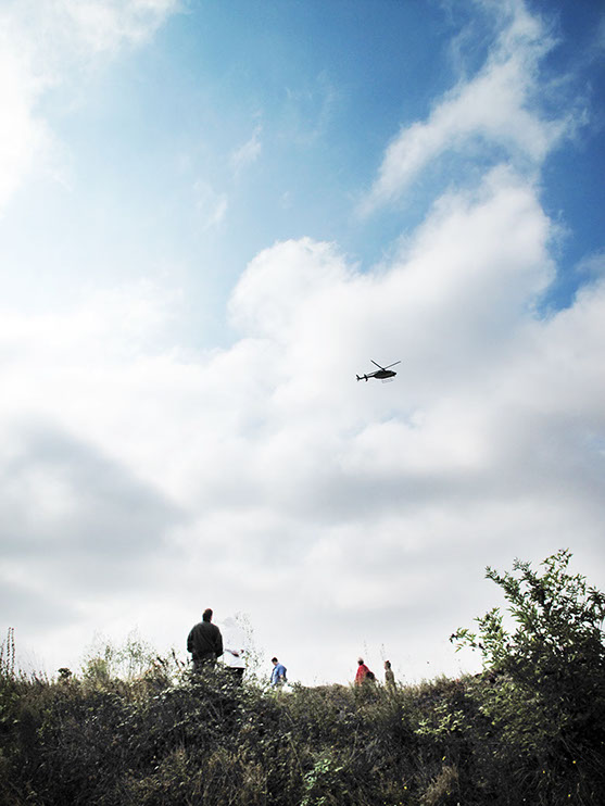 A Performer is flying in a Helicopter Bell 407 and looking at the exhibition from above for 2-3 minutes and then flying away.